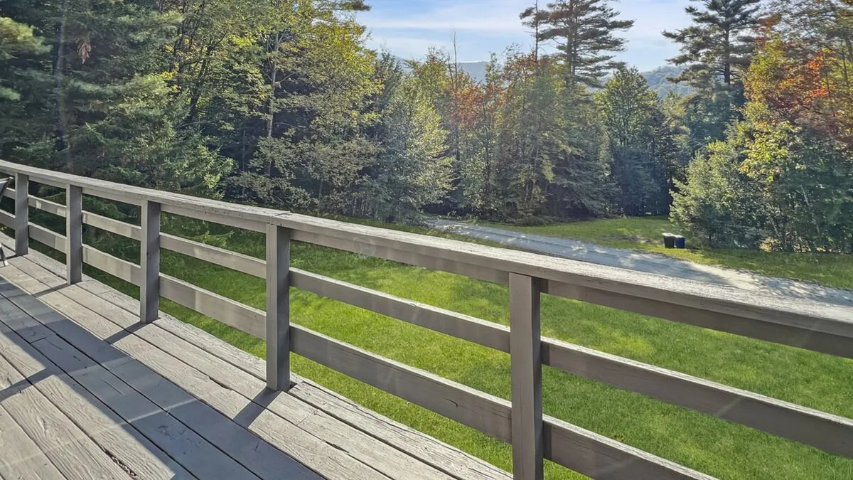 An upper deck bordered by a sturdy wooden railing, surrounded by lush green grass and trees. The deck offers a private outdoor retreat, ideal for grilling or simply soaking up the mountain air and scenery.