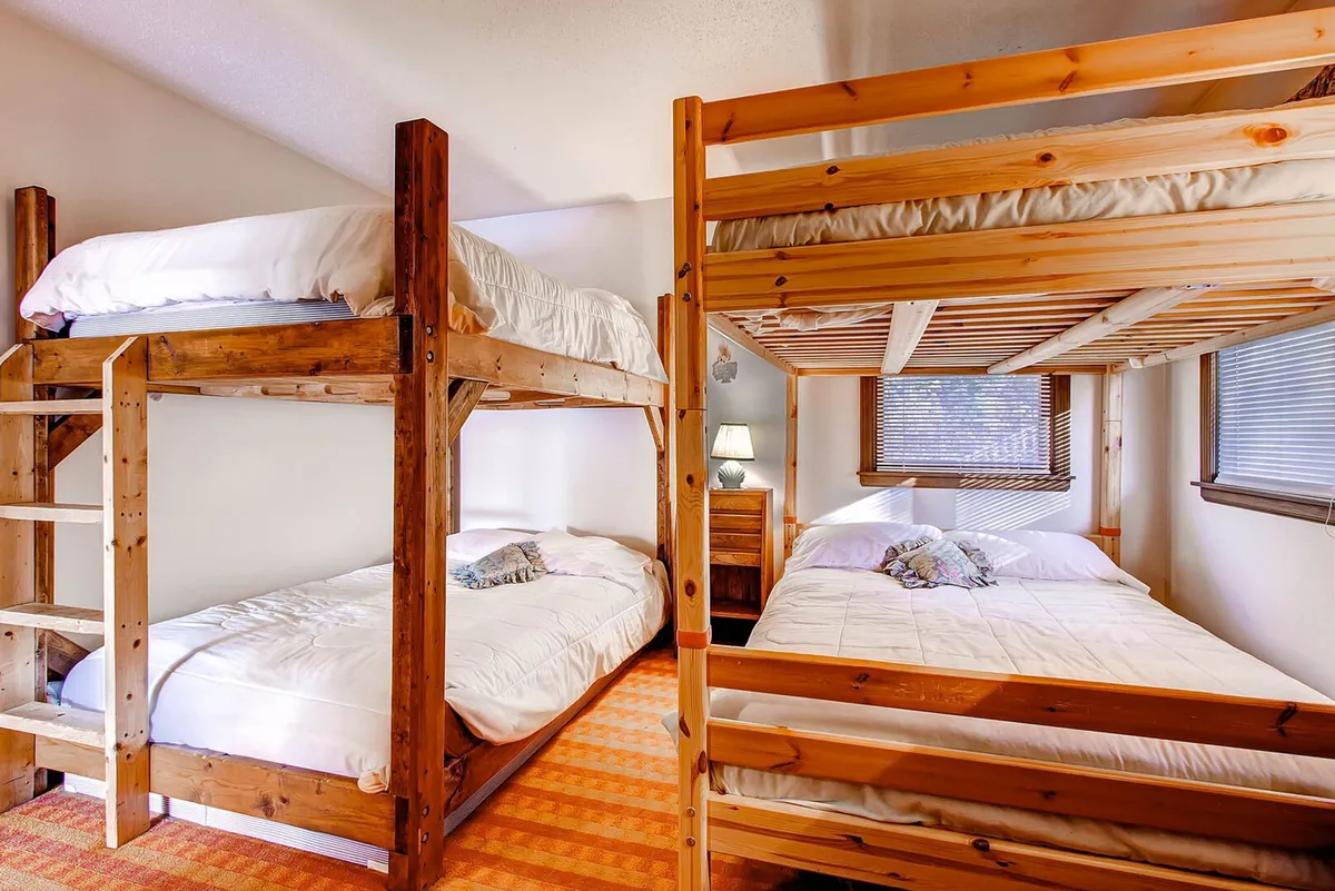 A welcoming bunk bedroom with both bunk beds and a double bed, complemented by a bedside lamp and a plush rug. The arrangement offers a flexible sleeping solution for different group sizes and ages, fostering a sense of shared experience and closeness.