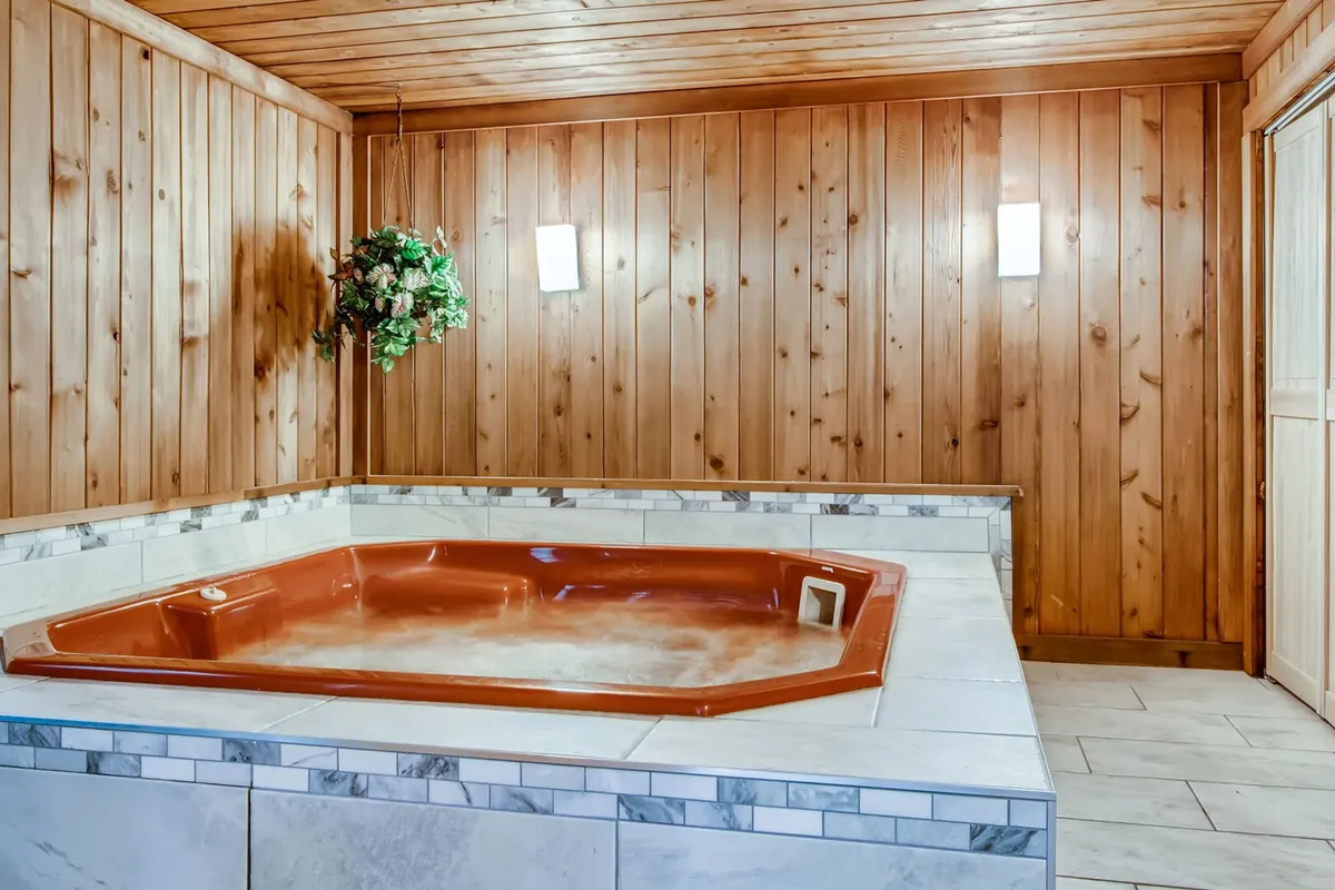 This image showcases an inviting indoor jacuzzi surrounded by warm wood paneling, with a decorative plant adding a touch of freshness and soft light fixtures creating a tranquil ambiance. The spacious setup hints at a luxurious, spa-like retreat perfect for post-adventure relaxation.