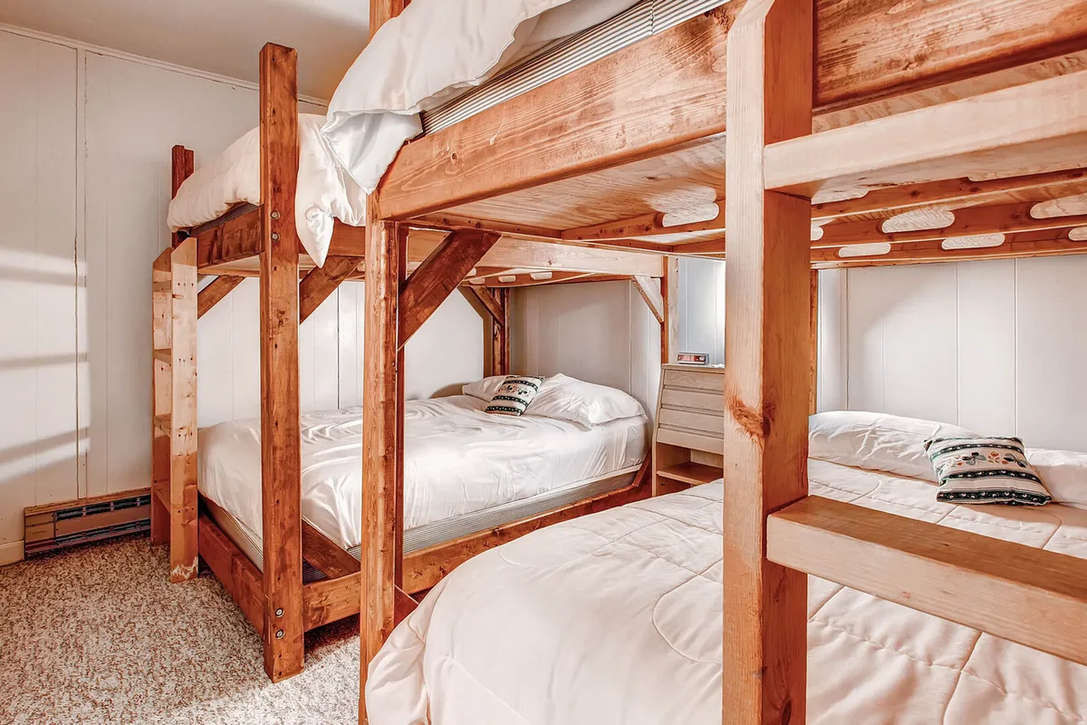 A vibrant bedroom featuring full-size bunk beds dressed in cozy linens and decorative pillows. The room exudes a playful and relaxed vibe, evoking memories of sleepovers and group bonding. Soft lighting and ample space for guests make it perfect for families or friends sharing the space.