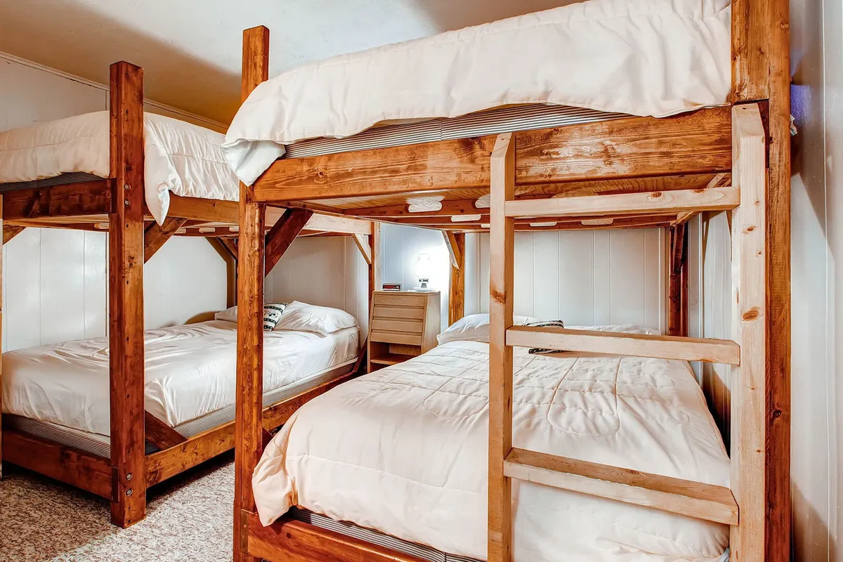 This image features a cozy bunk bed setup with wooden furniture and inviting bedding, evoking a sense of warmth and comfort. The space hints at both practicality and playful relaxation, making it ideal for families and groups after a day of adventure.