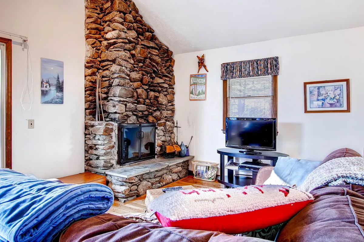 A cozy living area centered around a rustic stone fireplace, with a comfortable couch, decorative wall art, and ambient lighting. The scene suggests a welcoming gathering spot for relaxation and socializing after outdoor activities.